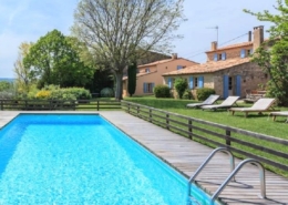 Large swimming pool in foreground showing sunloungers and garden with Provencal villa in the background.