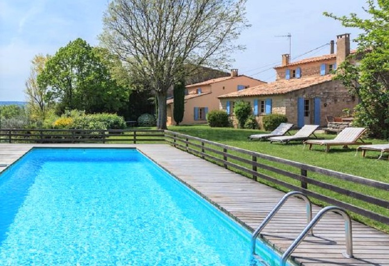 Large swimming pool in foreground showing sunloungers and garden with Provencal villa in the background.