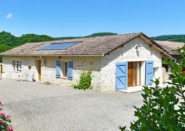 Renovated barn holiday rental gite with white stone walls and blue shutters, located in a pretty yard with shrubs