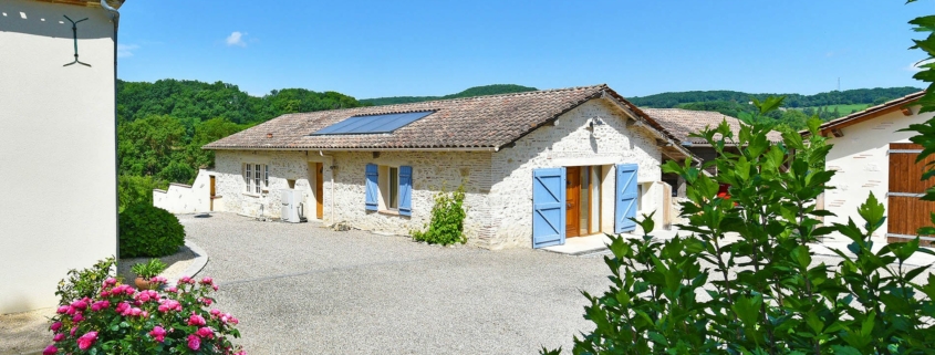 Renovated barn holiday rental gite with white stone walls and blue shutters, located in a pretty yard with shrubs