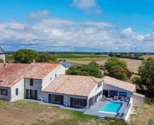 Aerial view of large house with tiled roof and swimming pool set in beautiful countryside of Charente-Maritime, France