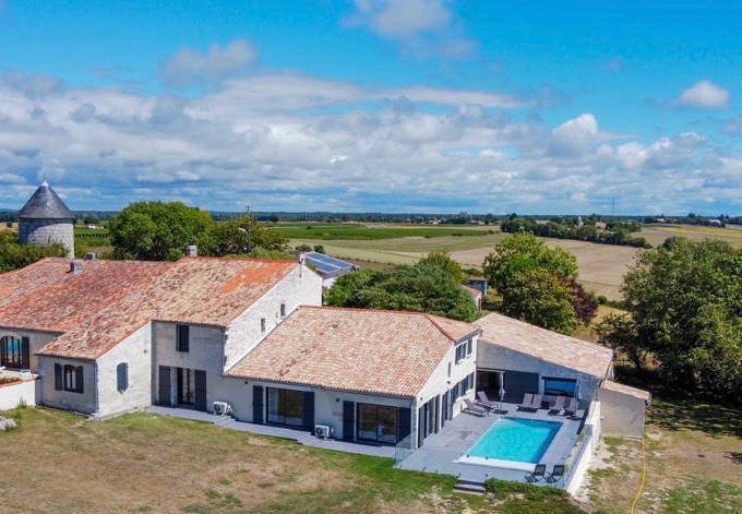 Aerial view of large house with tiled roof and swimming pool set in beautiful countryside of Charente-Maritime, France