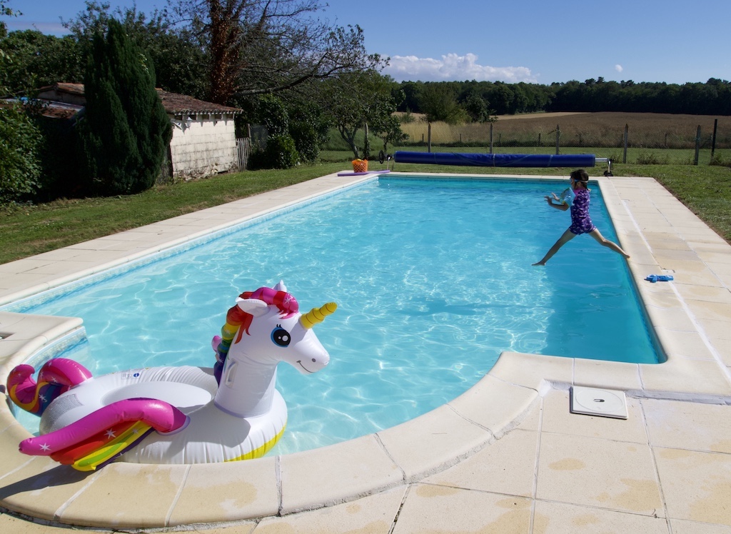 Turquoise swimming pool with unicorn float and child jumping in.