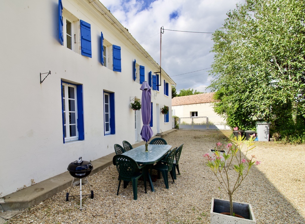 Side view of La Bigorre Farmhouse - white stone walls with blue shutters on each window. Terrace area showing outdoor seating