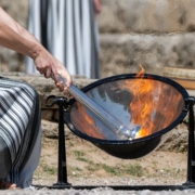 Lady in old style grecian clothing, lights the Olympic flame from the sun's rays in a mirrored cauldron