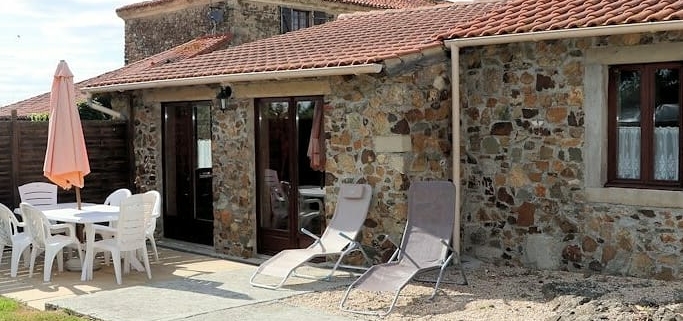 View of French gite with terracotta tiled roof and traditional stone walls. Patio area with sunloungers and table & chairs