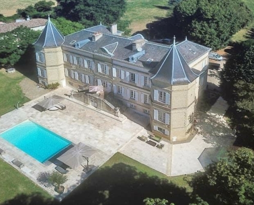 Aerial view of French Chateau with two turrets and view of swimming pool.